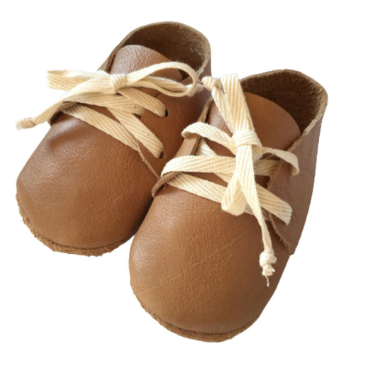 Pair of tan leather baby shoes with cotton laces on a white background