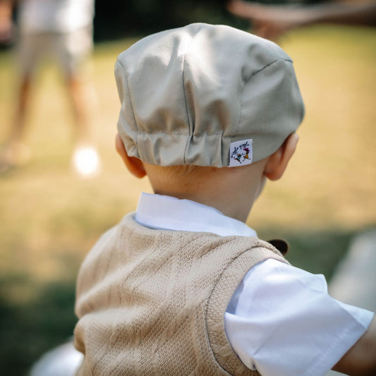 Baby boy wearing a tan flap cap from the back showing the elastic in the hat