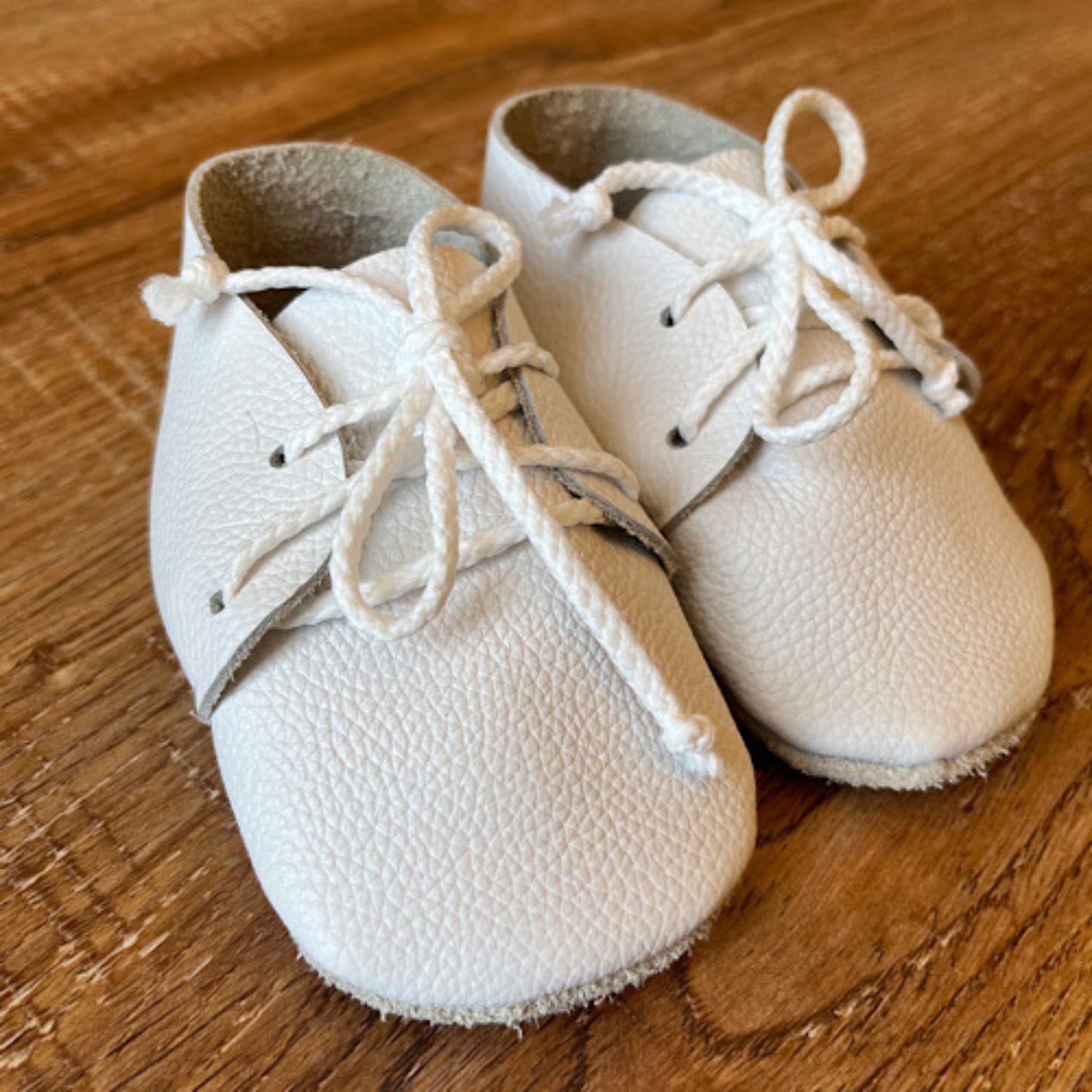 Pair of white baby shoes with laces on a wooden surface