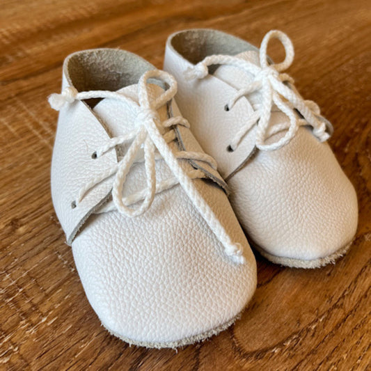 Pair of white baby shoes with laces on a wooden surface
