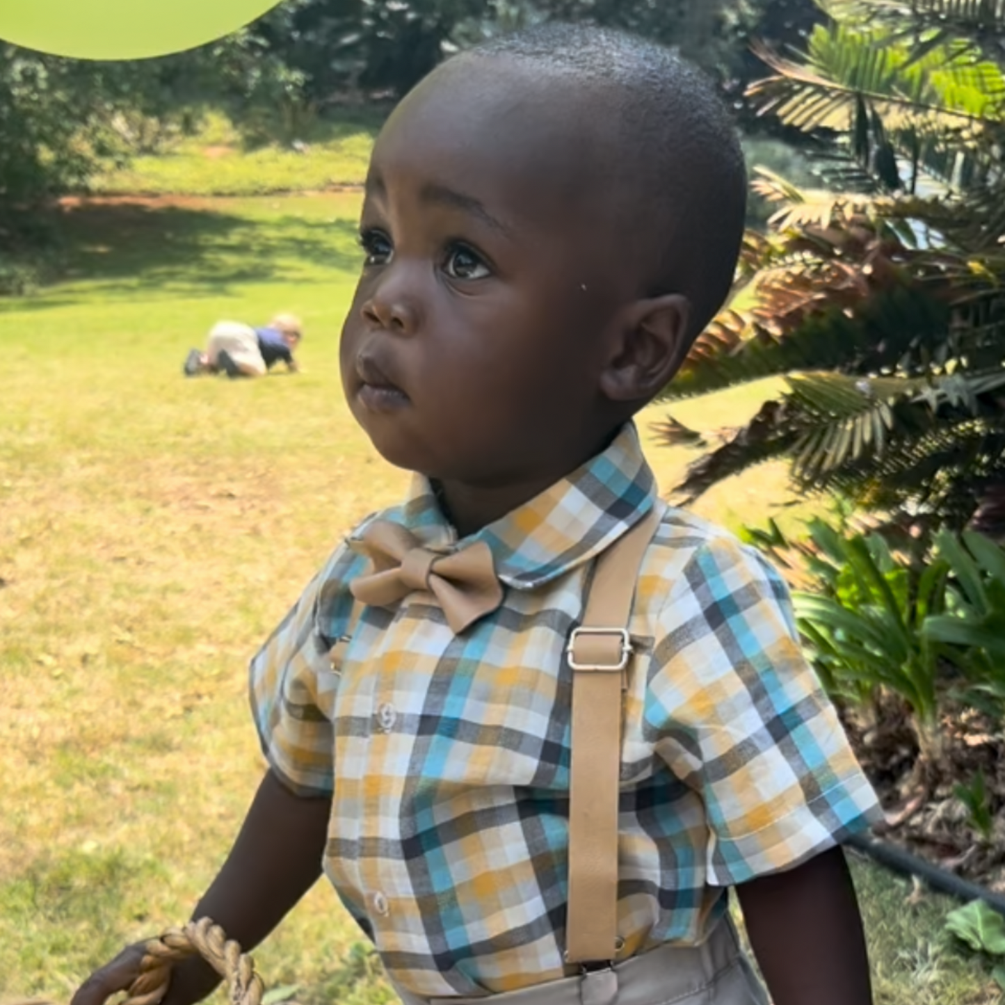 Baby boy wearing a check shirt with leather bow tie and suspenders outdoors
