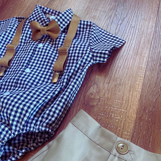 Baby Boy Blue and white checkered shirt with leather suspenders and a leather bow tie on a wooden surface