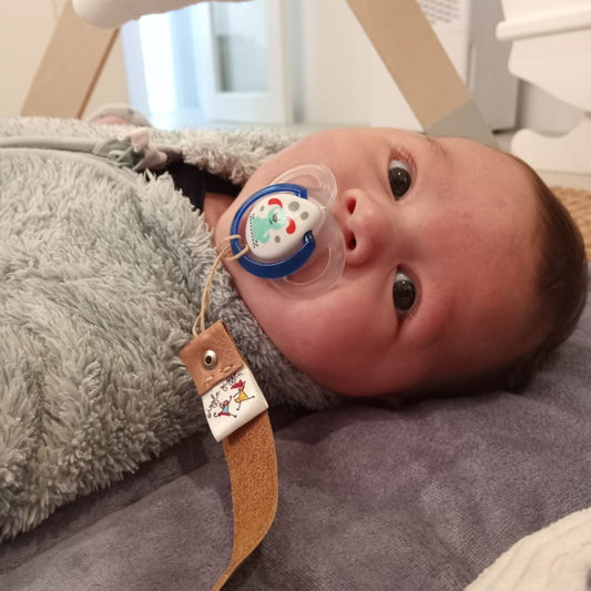 Baby sucking on a pacifier with a leather strap in a crib