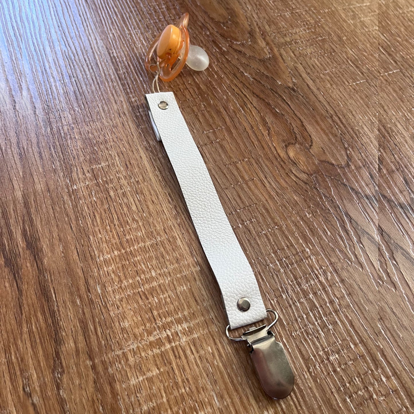 White leather pacifier strap with a clip on a wooden surface