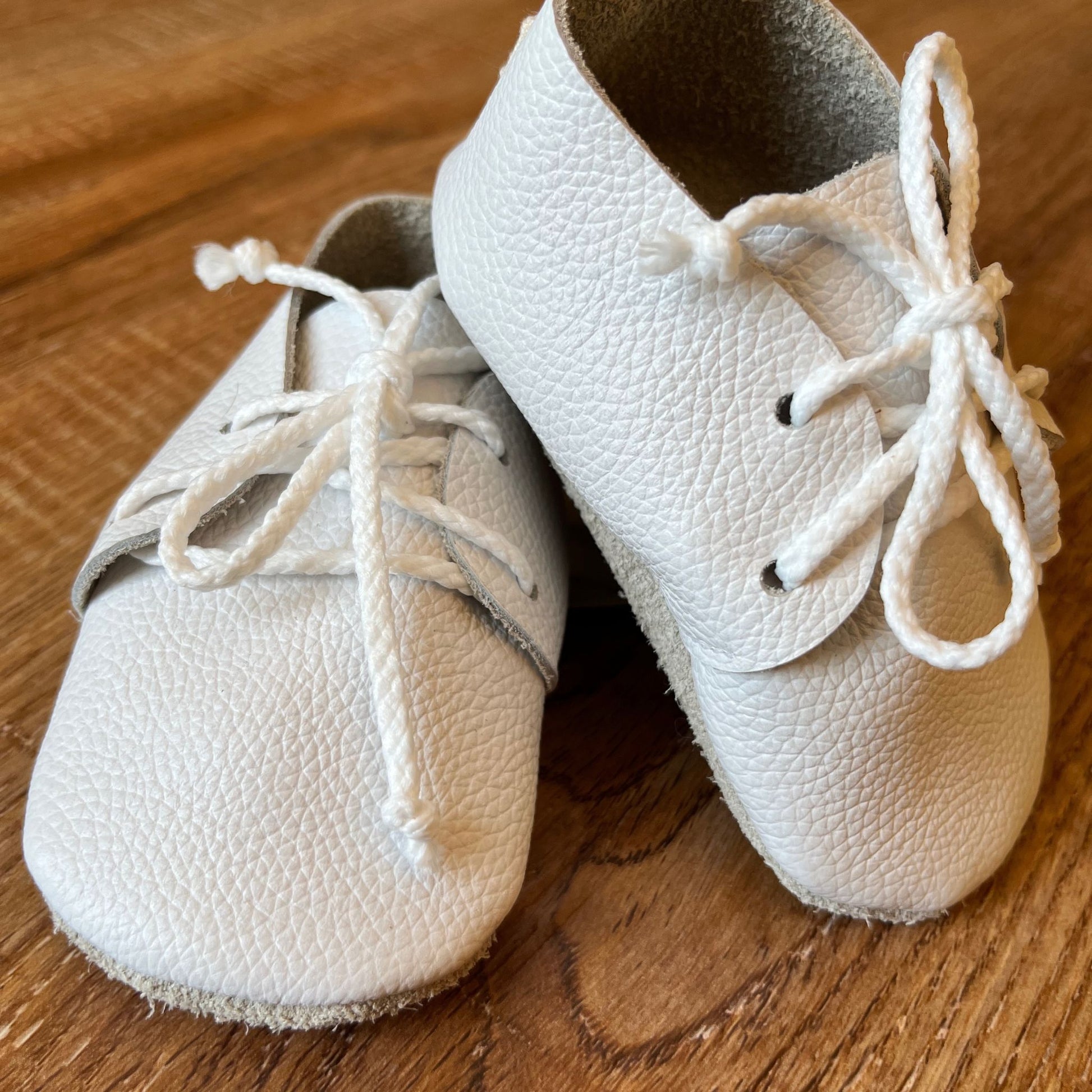 Pair of white leather baby shoes with laces on a wooden surface