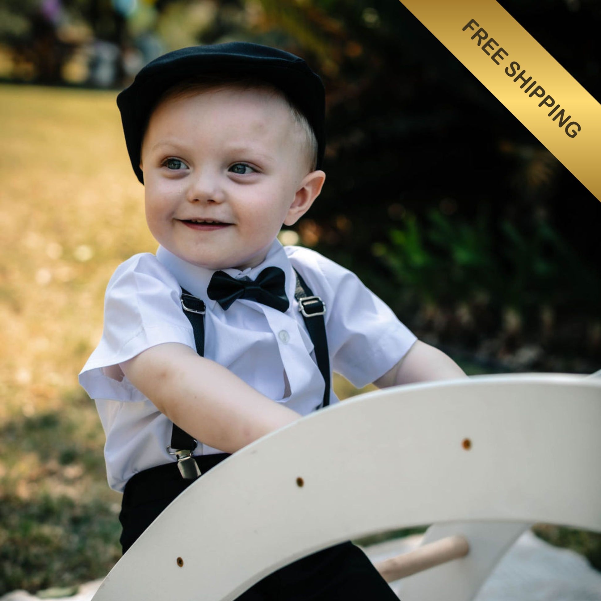 Baby boy in formal attire with black leather suspenders and bow tie, sitting on a wooden toy.