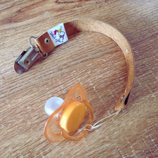 Orange pacifier with a tan leather strap on a wooden surface