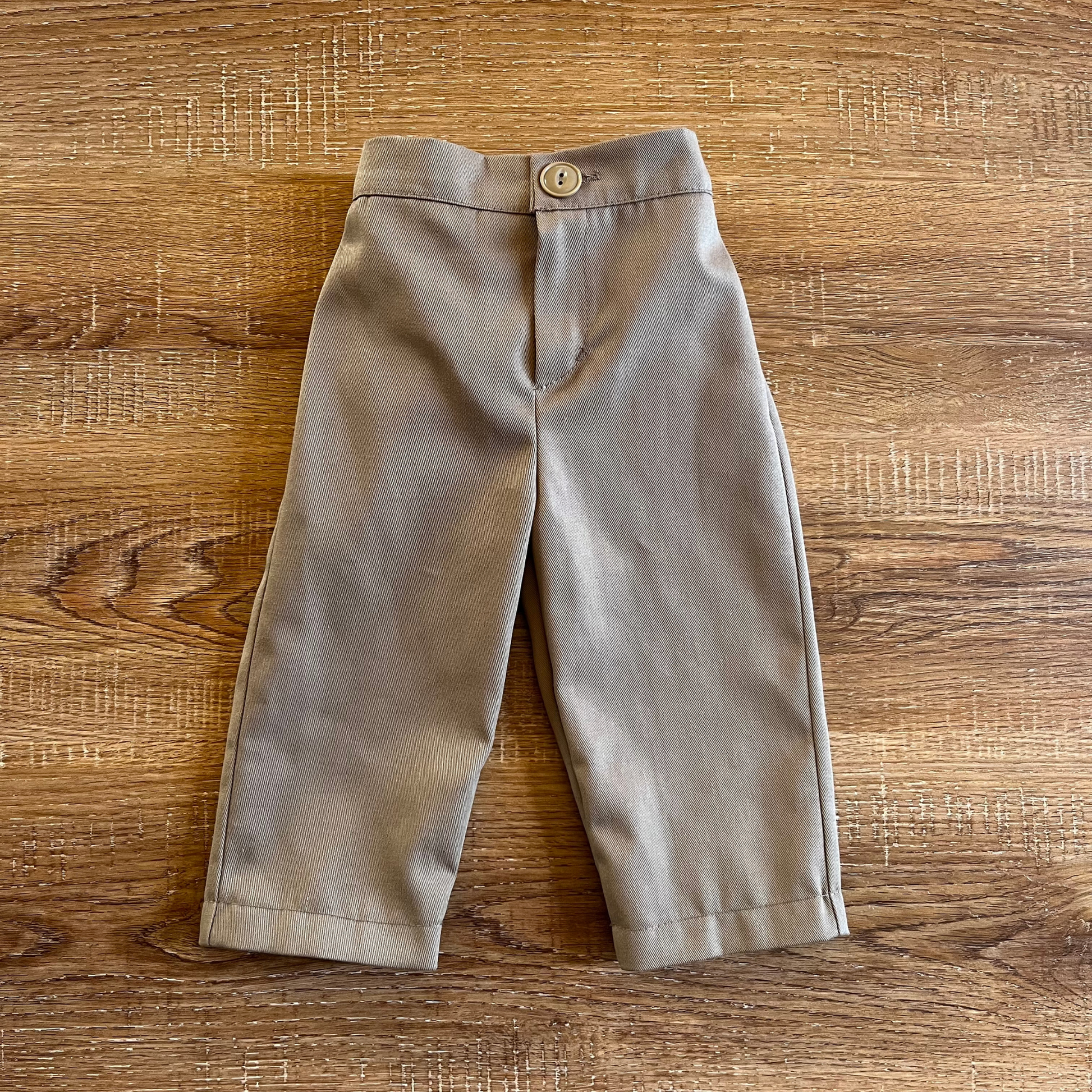 Tan baby boy chino trousers on a wooden surface
