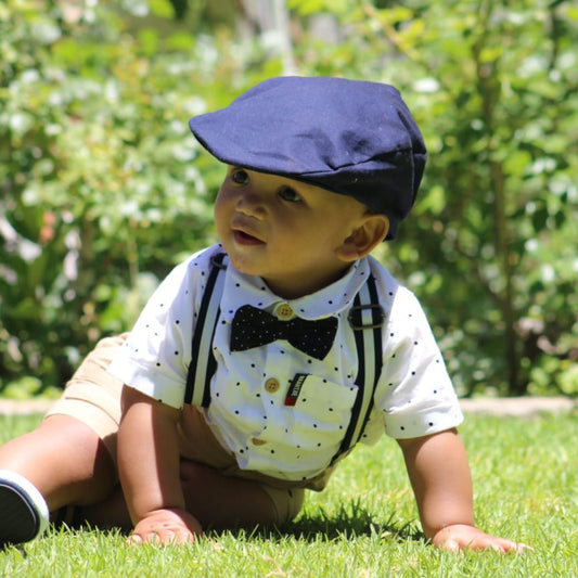 Baby boy in formal outfit with navy flat cap sitting on grass