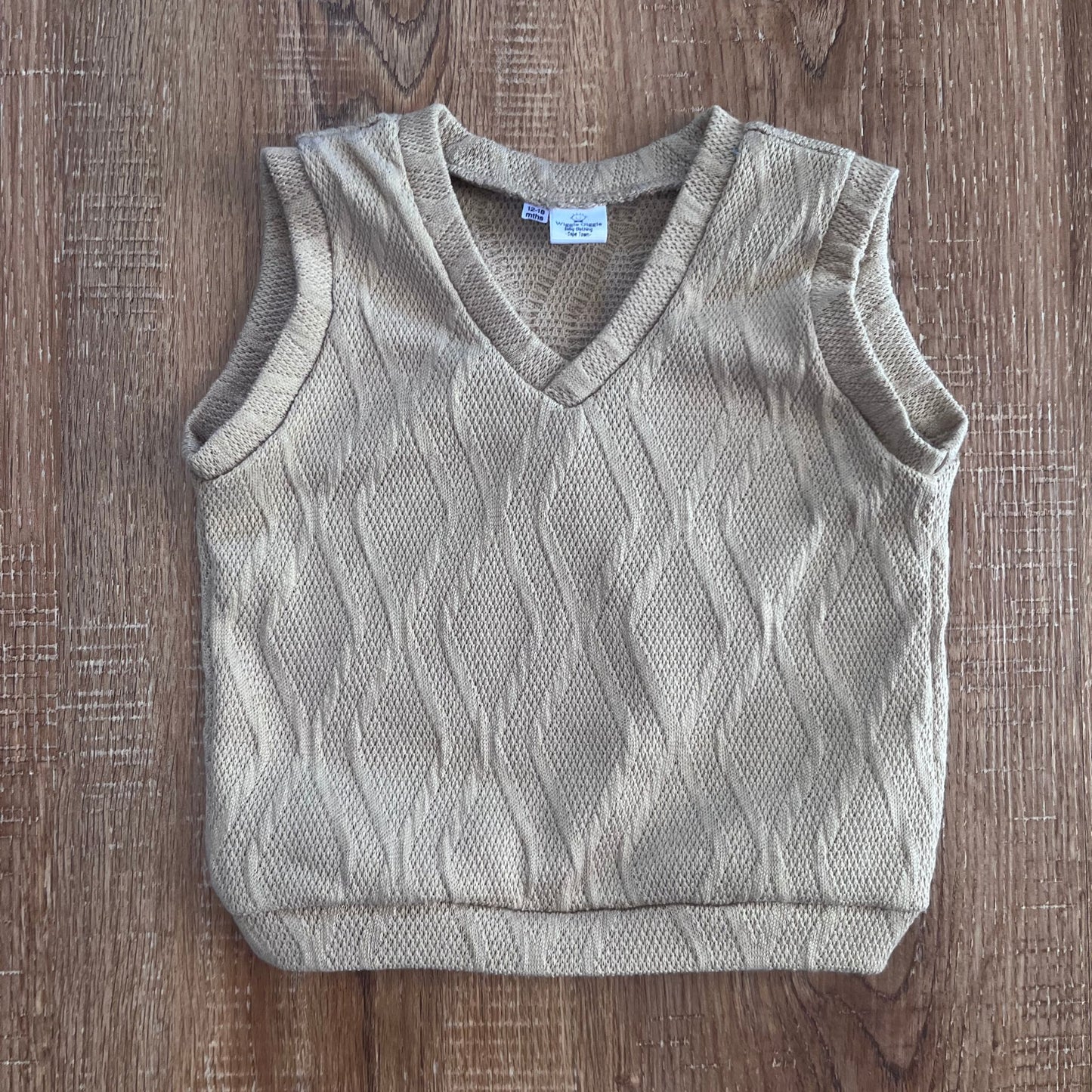 Light brown knitted baby boy vest on a wooden surface