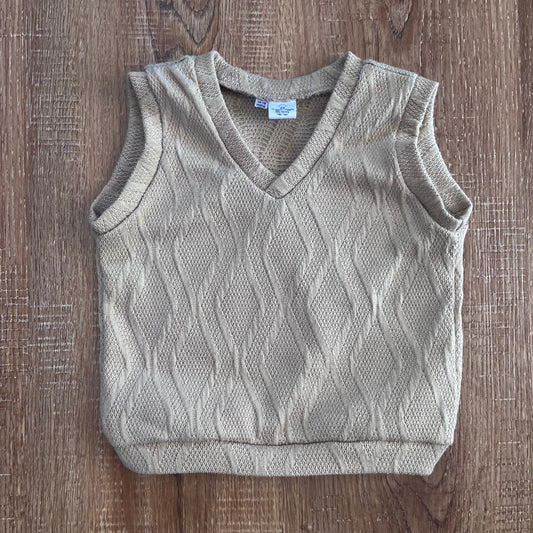 Light brown knitted baby boy vest on a wooden surface