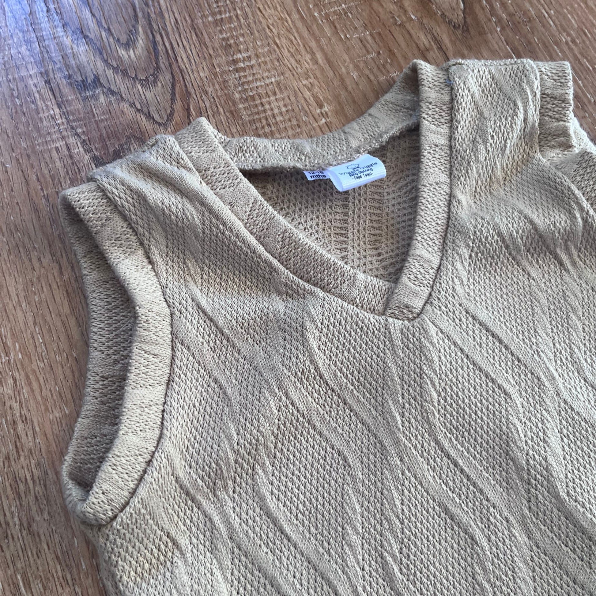 Beige sleeveless knit vest on a wooden surface