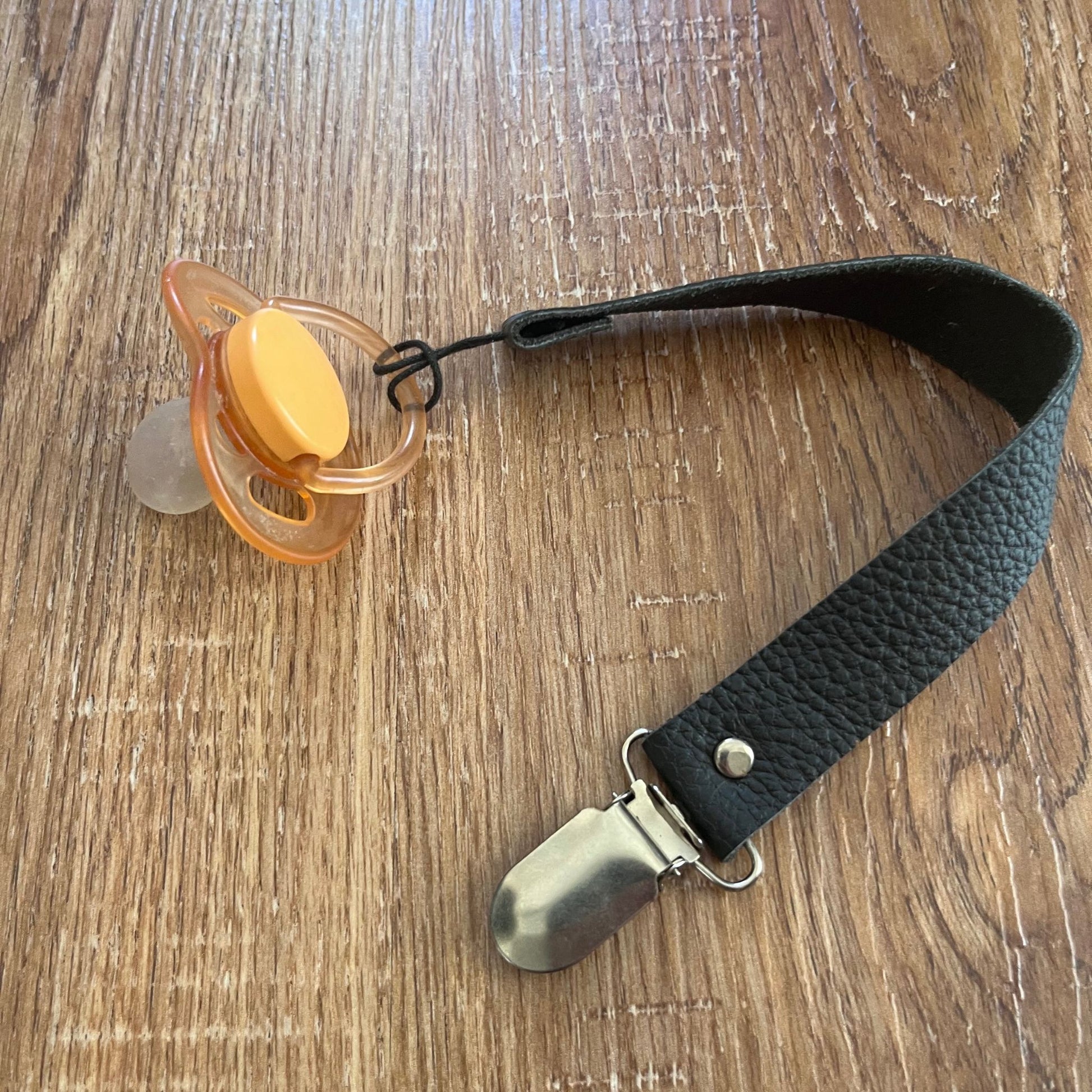 Orange pacifier with a black Leather pacifier strap on a wooden surface