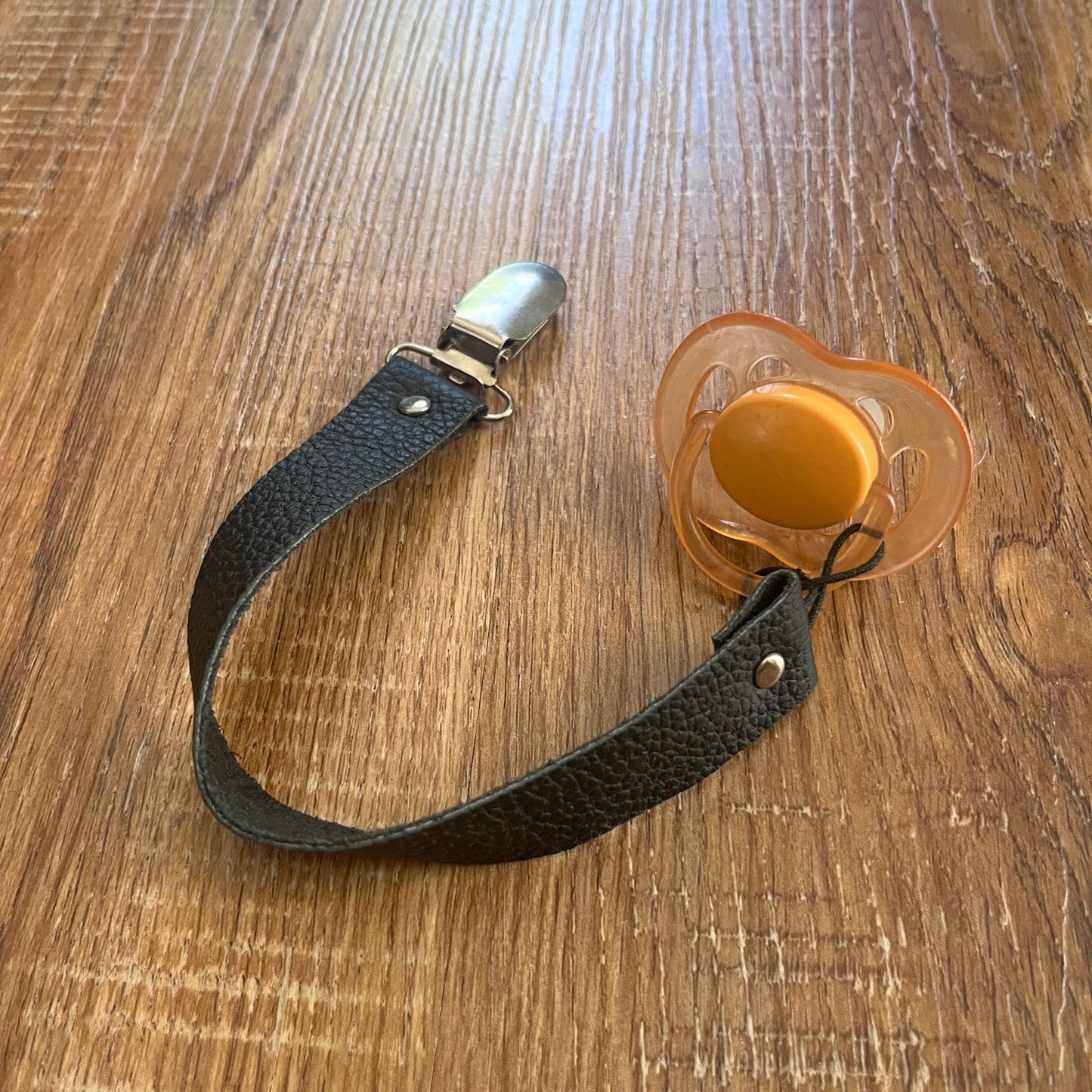 Leather baby pacifier with black strap on a wooden surface