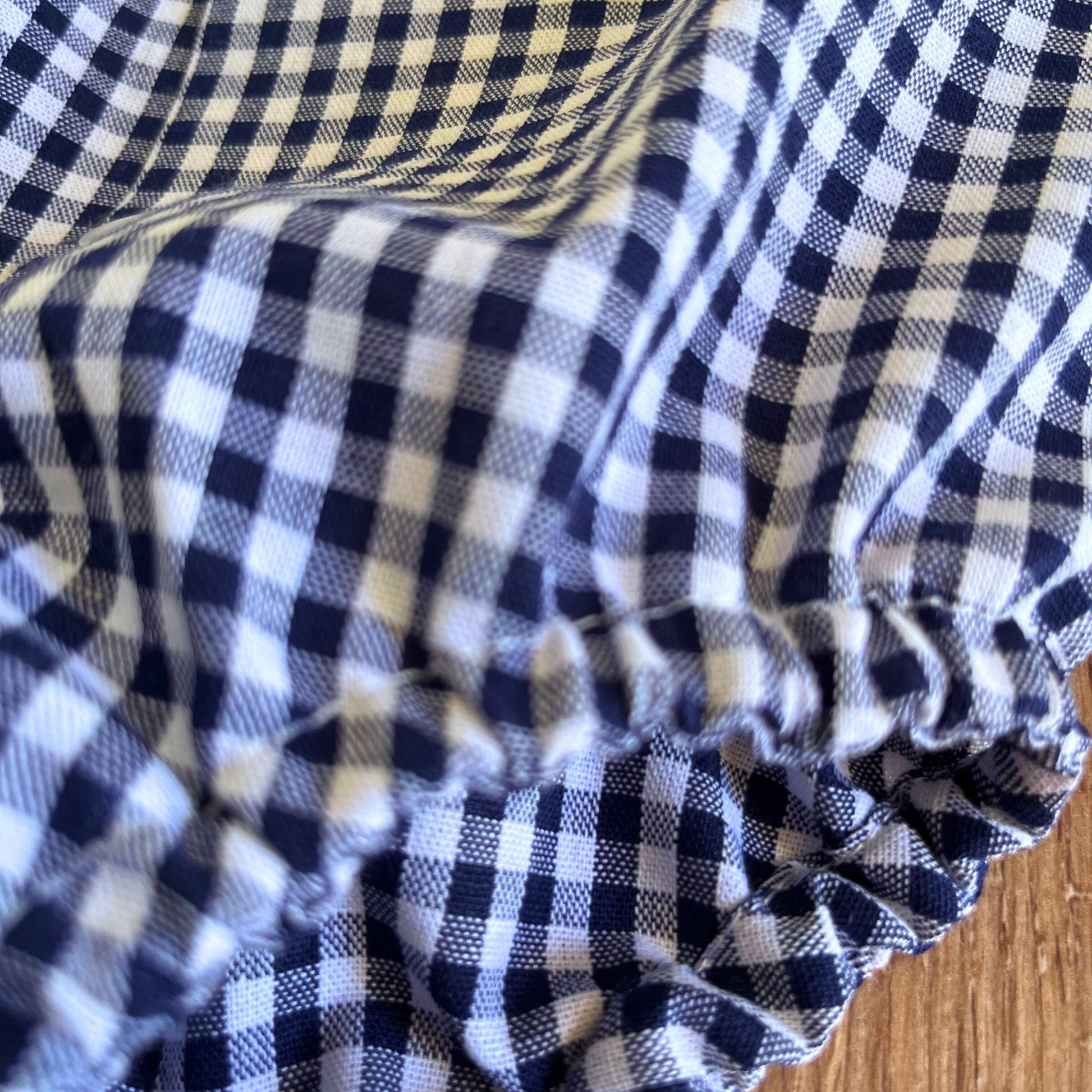 Close-up of blue and white checkered Baby Boy Romper on a wooden surface