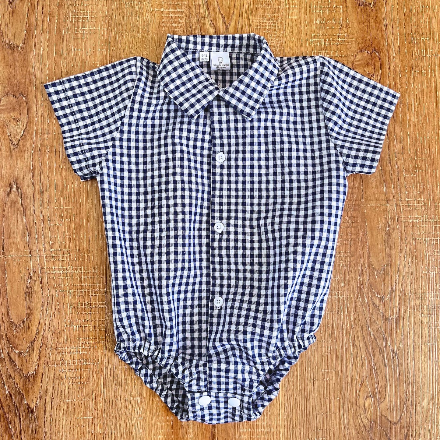 Blue and white checkered baby romper on a wooden surface