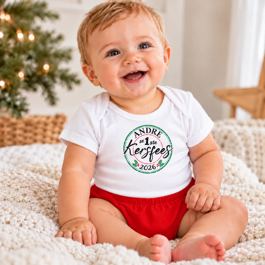 Baby boy sitting on a blanket smiling wearing a white onesie with his name on it and Eerste Kersfees with a red diaper cover