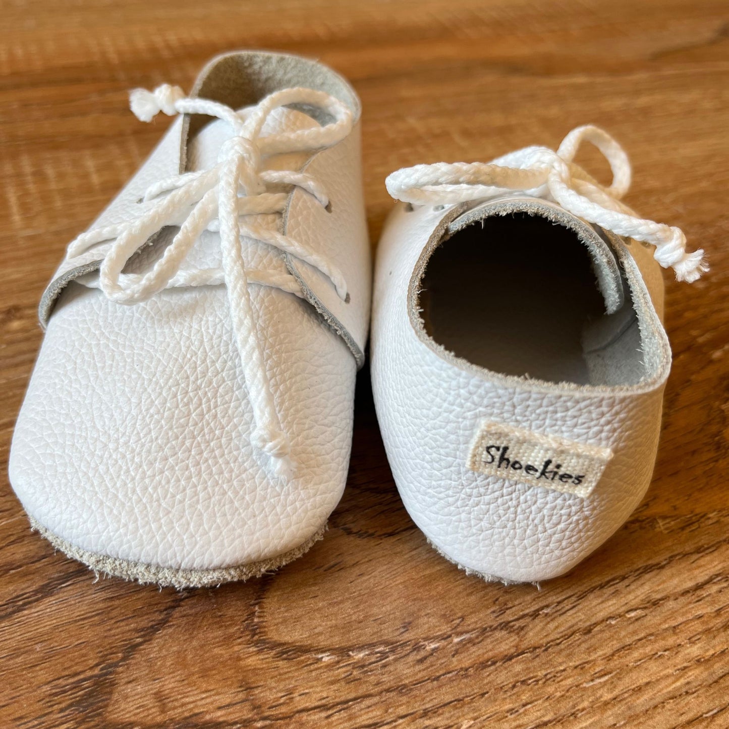 Pair of white baby shoes with laces on a wooden surface