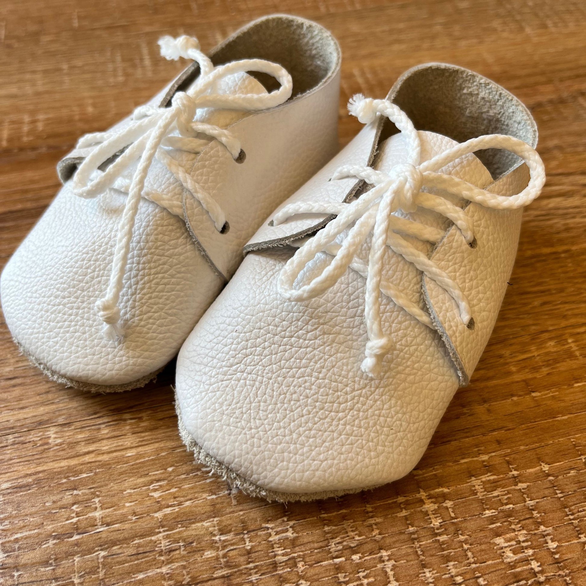 Pair of white baby shoes with laces on a wooden surface